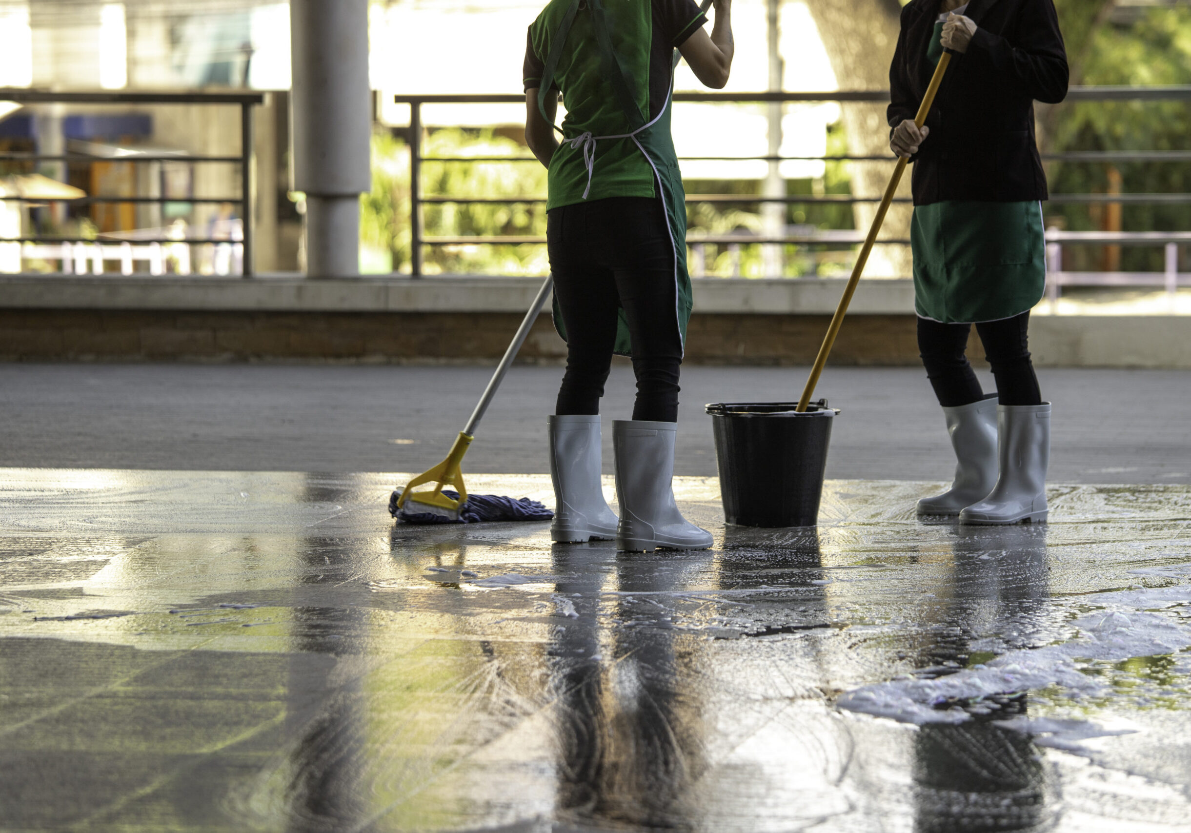 cleaner with mop and uniform cleaning hall floor of public business building