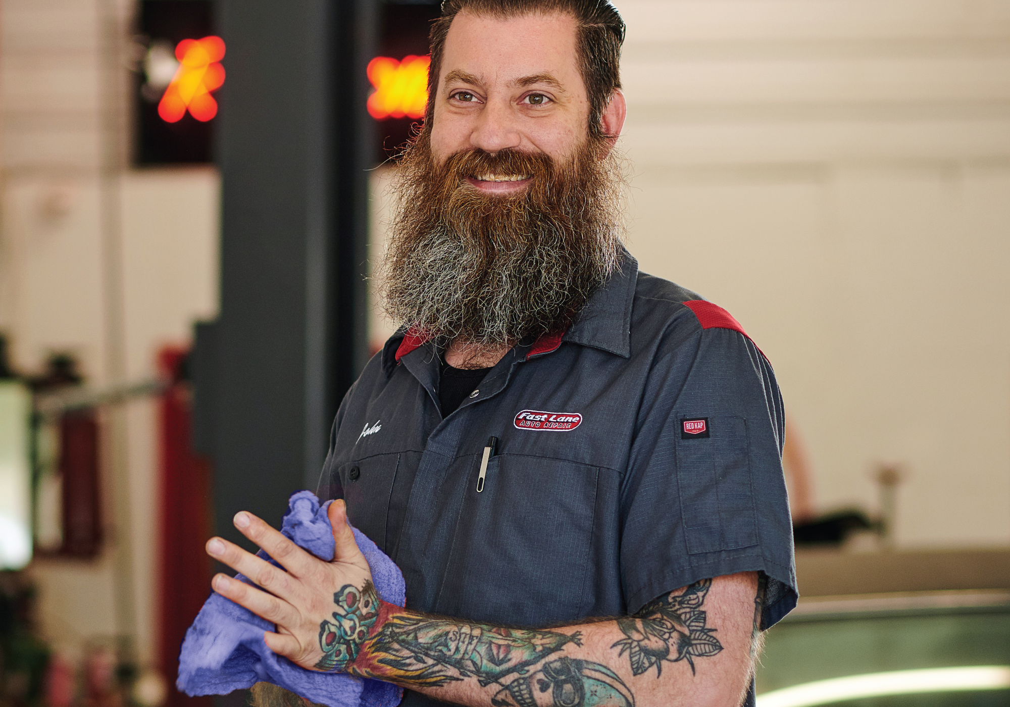 Mechanic using a blue shop towel wearing an automotive uniform